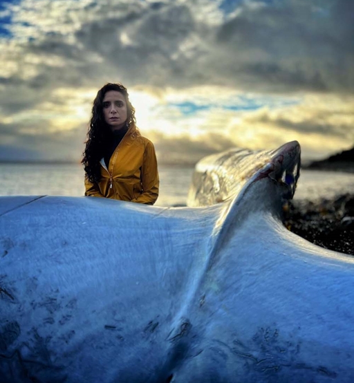 Woman standing at a stranded whale tail.