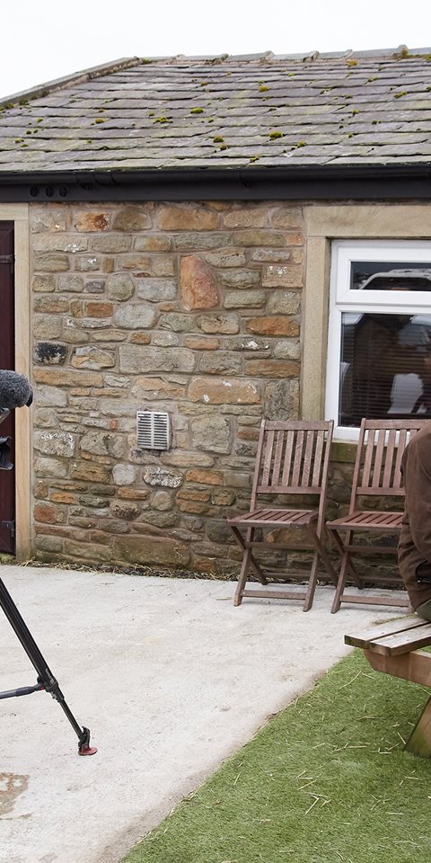 A cameraman shooting three people talking at an outdoor table.