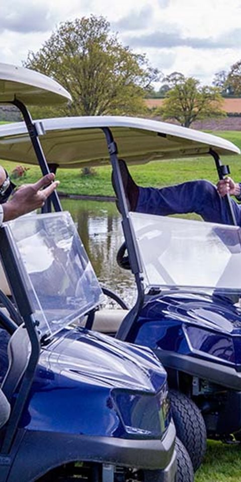 Two men standing on golf cars and smiling at the camera.