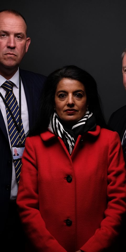 A woman and two men behind her standing and posing for the camera.