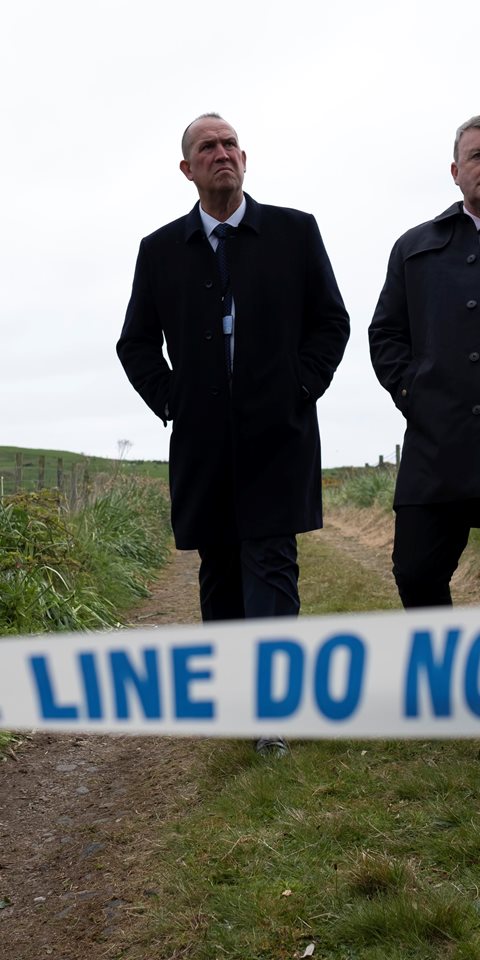 Two men standing in front of police tape outdoors.